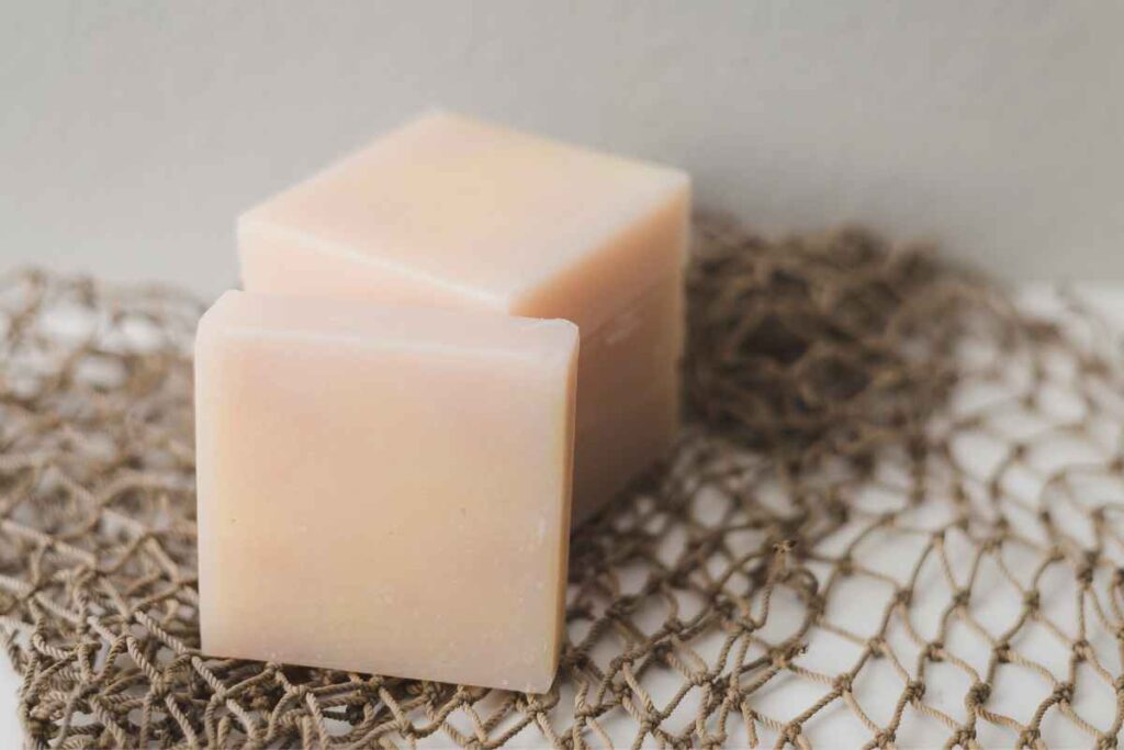 Two pale pink handmade soap bars placed on a piece of brown netting, providing a rustic and natural presentation.