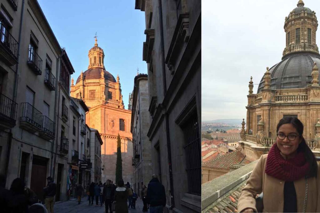 A stunning view of a historic cathedral bathed in golden light, towering over a narrow European street lined with classic buildings and pedestrians. On the right, a woman in a beige coat and burgundy scarf smiles while standing on a rooftop with a close-up view of the intricate cathedral dome and the cityscape of Salamanca in the background. Best day trips from Madrid.