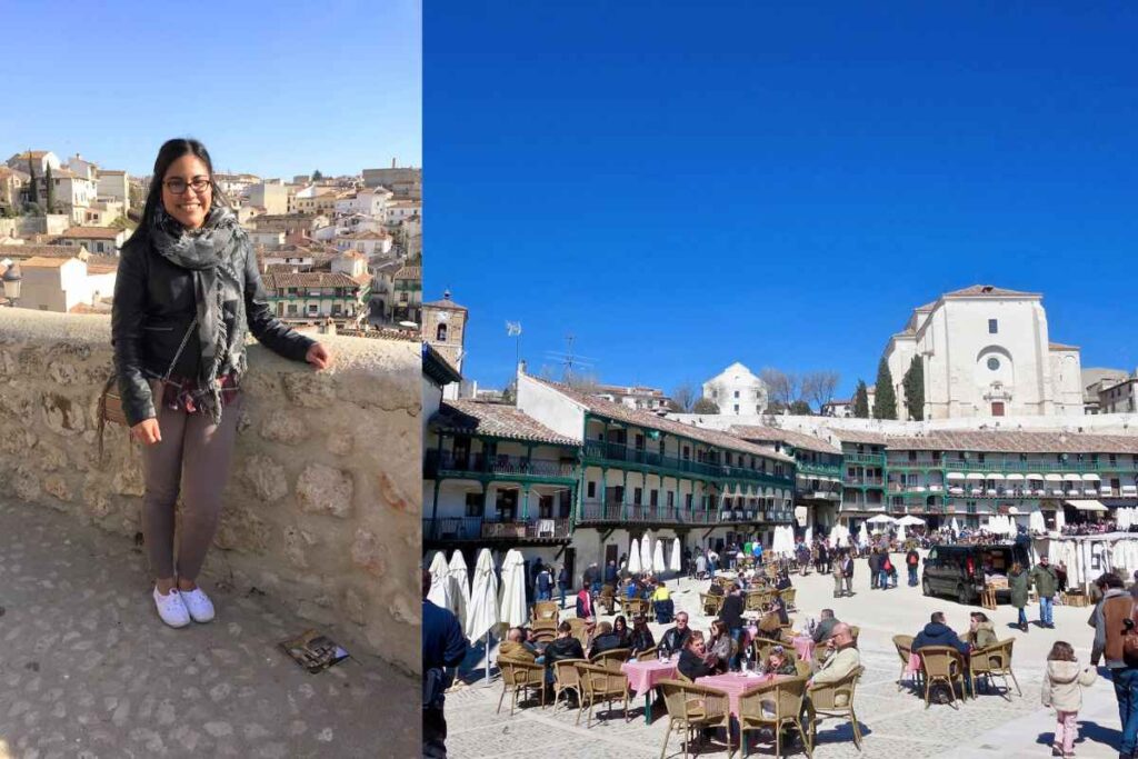 A smiling woman in a black leather jacket and gray pants poses against a stone wall, overlooking a picturesque town with white buildings and terracotta rooftops. On the right, an outdoor square with lively cafés, green balconies, and a bright blue sky. Best day trips from Madrid.