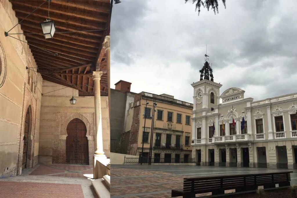 A covered passageway with a wooden-beamed ceiling and an arched doorway, reminiscent of traditional Spanish architecture. On the right, a white neoclassical town hall building with a clock tower, standing against a cloudy sky. Best day trips from Madrid.