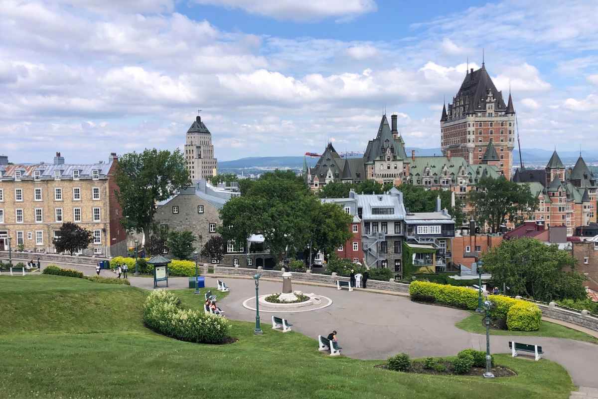 A panoramic view overlooking the historical buildings of Old Quebec City from Montmorency Park, showcasing a serene park with people relaxing on benches, surrounded by lush greenery, with the iconic Château Frontenac in the background. This is one of the best things to do in Old Quebec City, offering a peaceful retreat with a stunning backdrop.