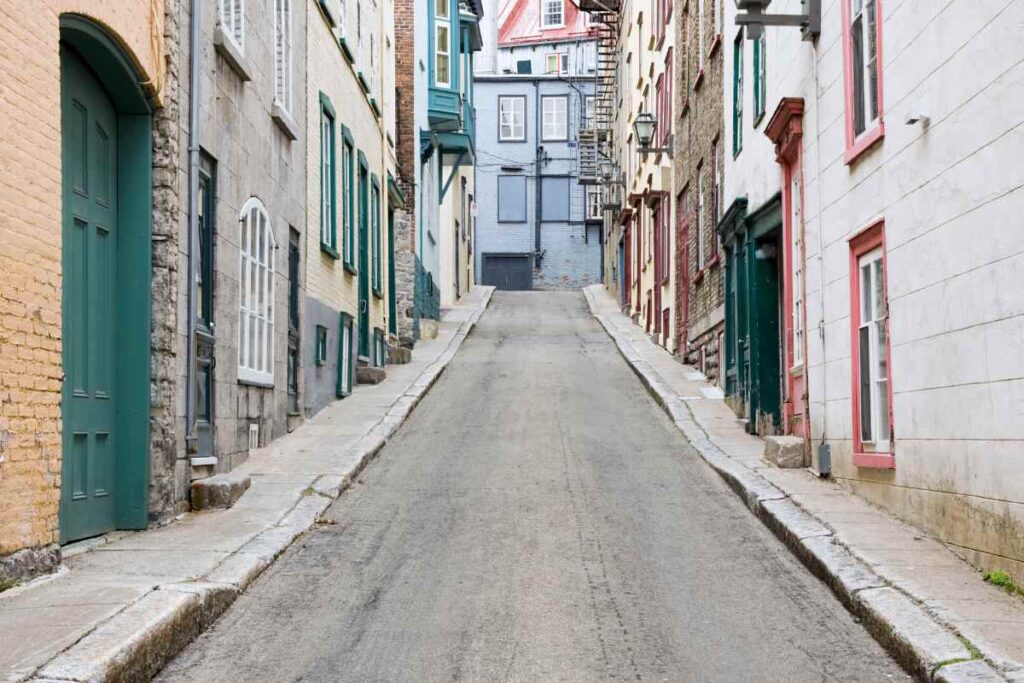 A picturesque, narrow street lined with historic buildings in Old Quebec City, showcasing colorful facades and traditional architectural details. This scene reflects the quaint atmosphere near the boutique hotels in Old Quebec City, where visitors can experience the city's unique charm and character.