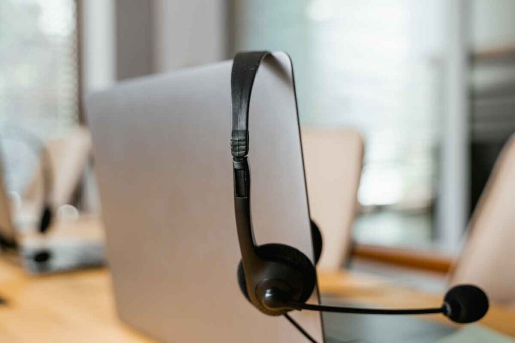 A black headset resting on a laptop in a modern office setting with neutral tones.