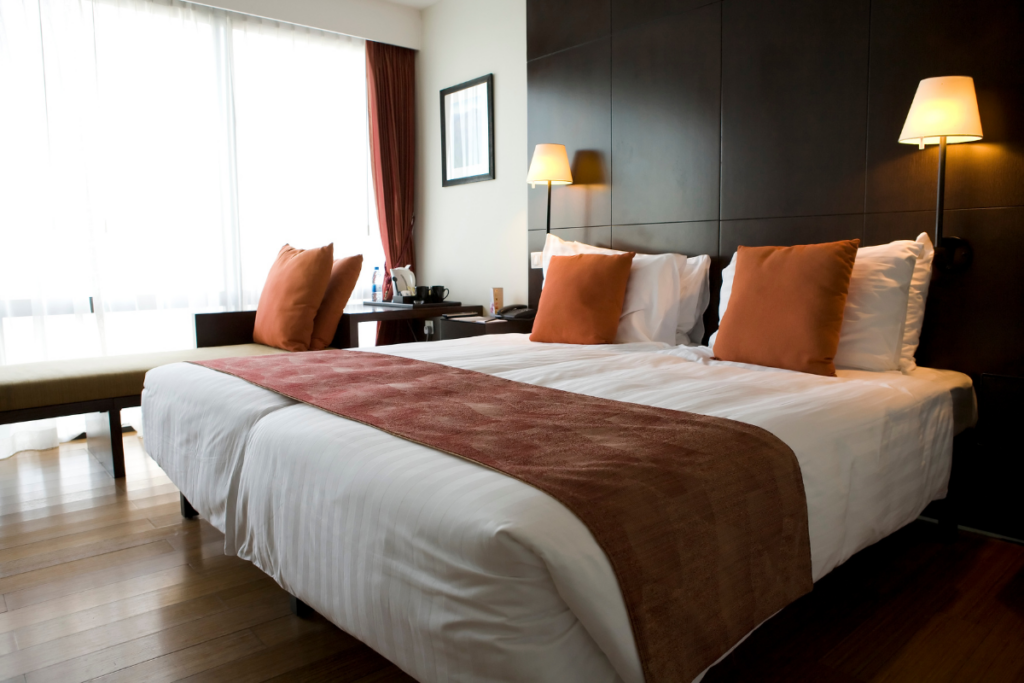 A cozy and stylish hotel room featuring a neatly made king-sized bed with crisp white linens, warm-toned pillows, and a soft decorative runner. Modern bedside lamps and a sleek dark wood headboard create a luxurious yet inviting atmosphere, perfect for a stay in one of the boutique hotels in Old Quebec City.