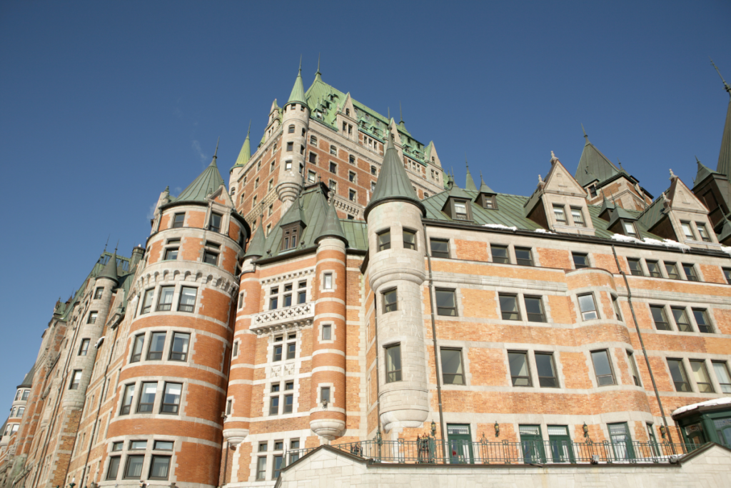 A stunning view of Château Frontenac, one of the most famous landmarks near boutique hotels in Old Quebec City. Its grand castle-like architecture with green rooftops and red brick walls stands against a clear blue sky.