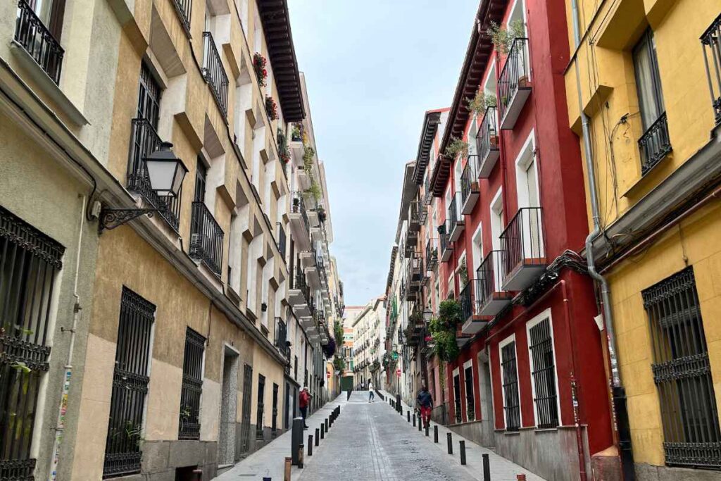 Narrow street in Madrid with colorful buildings and wrought iron balconies. A charming location to explore for those wondering where to stay in Madrid for the first time.