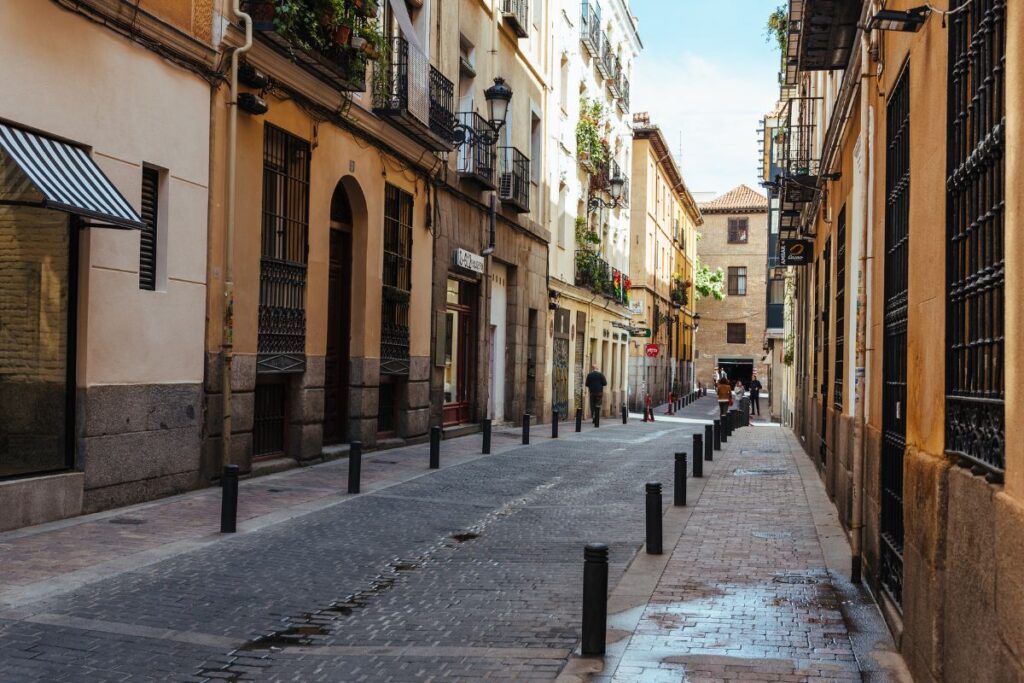 A charming street in Madrid lined with colorful buildings featuring balconies, plants, and traditional iron railings. A perfect place to explore for first-time visitors looking for an authentic stay in the city. Where to stay in Madrid for the first time.